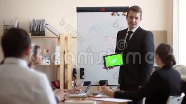 白种人穿着夹克和领带，手里拿着一个<strong>绿</strong>色<strong>屏</strong>幕的平板电脑，站在白板旁边，拿着一个<strong>绿</strong>色<strong>屏</strong>幕